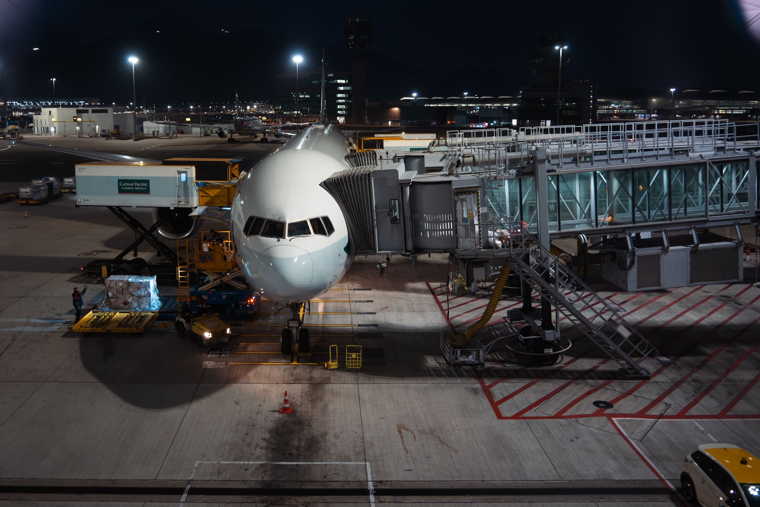 Wide-body aircraft parked at an airport gate at night, with a jet bridge and cargo loaders alongside